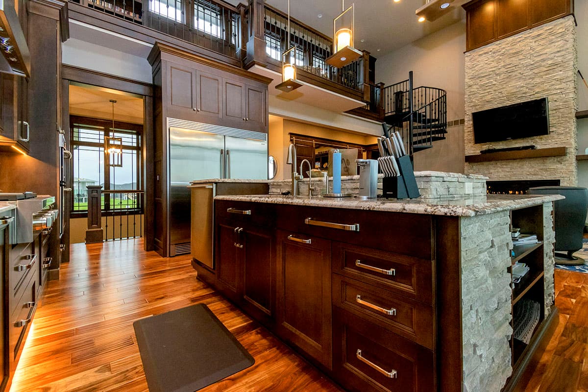 Interior view of a spacious kitchen with a large island, stainless steel appliances, stone fireplace, and spiral staircase.