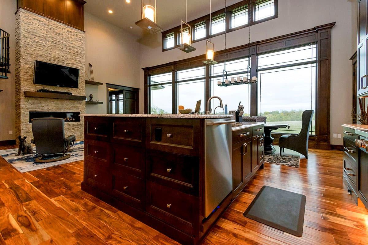 Interior rendering of a great room with a large stone fireplace, dark wood island, and expansive windows.