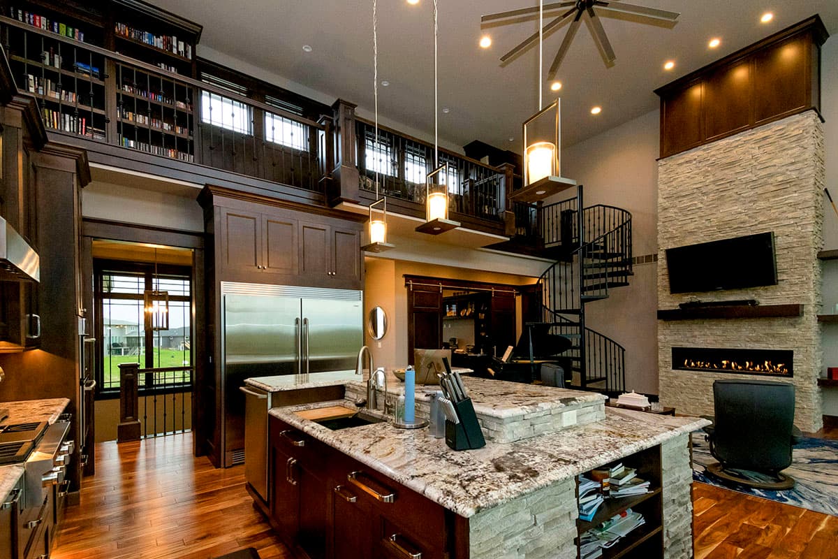 Open-concept living space with a kitchen island, spiral staircase, and stone fireplace with mounted TV.