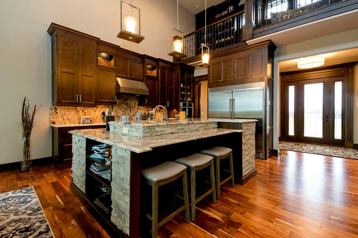 Interior view of a kitchen with a large island, dark wood cabinetry, granite countertops, and a mezzanine balcony above.