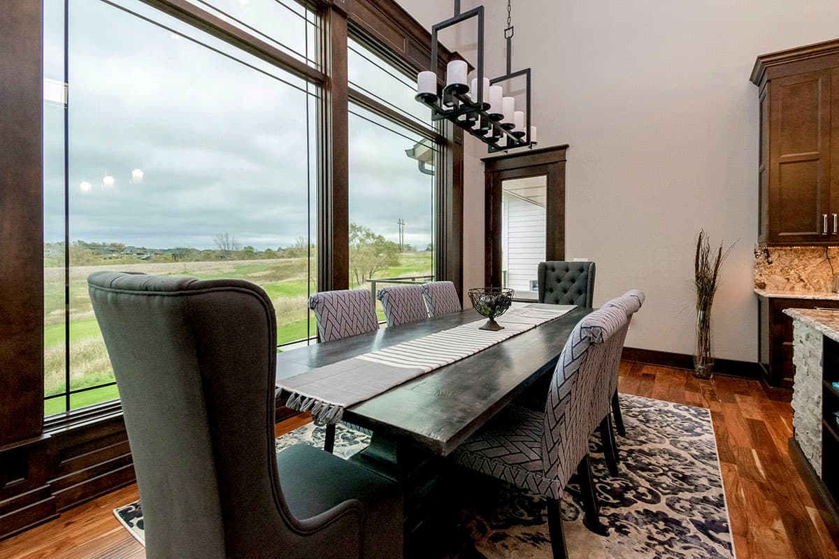 Dining room with large windows, dark wood accents, a rectangular table set for six, and a multi-tiered chandelier.