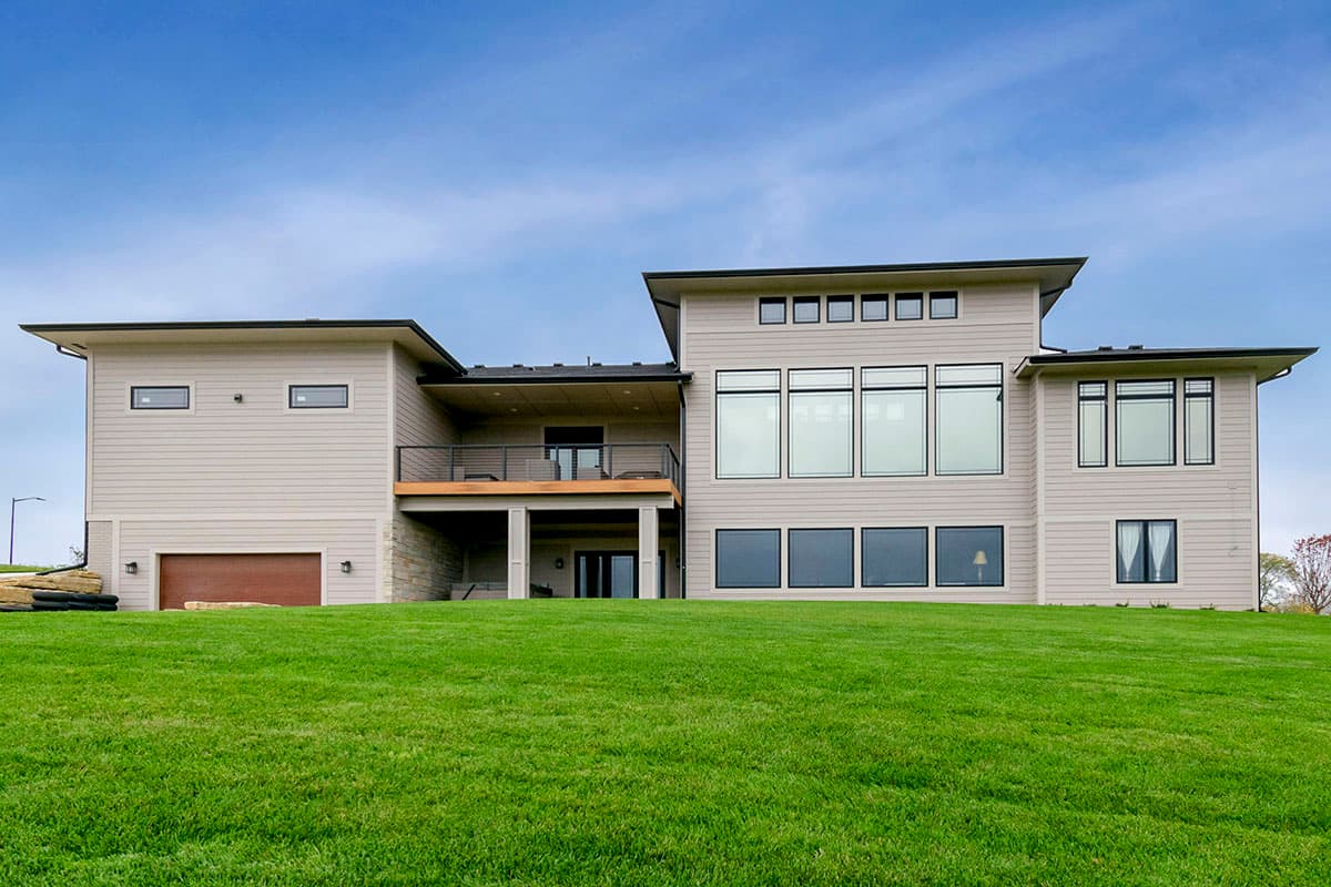 Modern house plan exterior with horizontal siding, cantilevered deck, large windows, and a three-car garage.