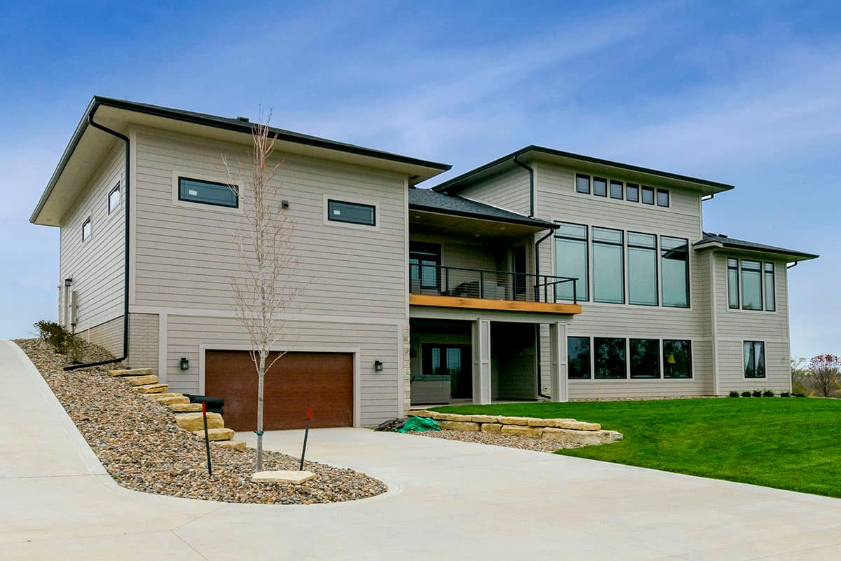Modern two-story house plan exterior with horizontal siding, a covered balcony, large windows, and a multi-car garage.