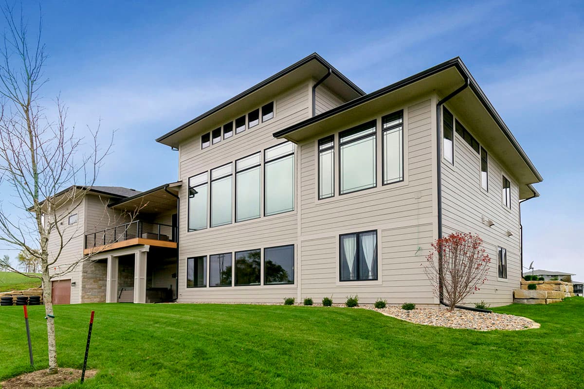 Modern two-story house plan exterior with large windows, gabled rooflines, and a covered deck.