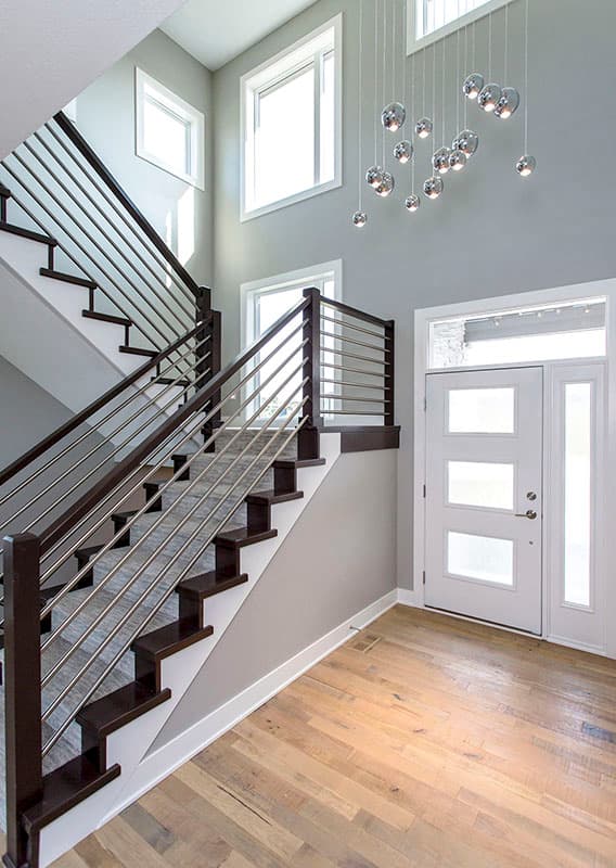 Interior foyer with floating staircase, horizontal railings, modern light fixture, and frosted glass entry door.