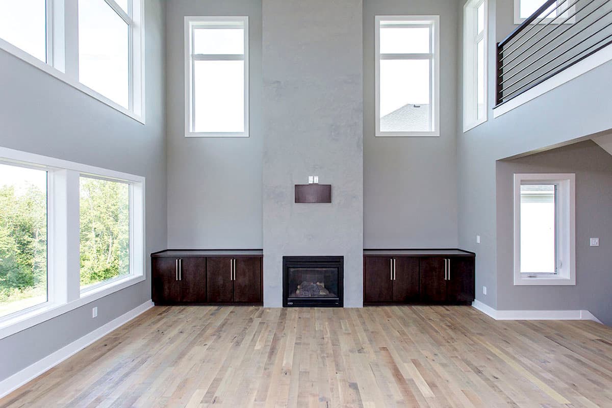 Great room with two-story windows, fireplace, built-in cabinets, and light wood flooring.