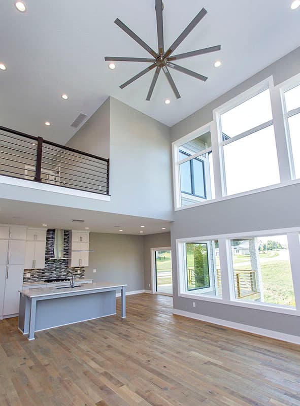 Modern house interior with open layout, kitchen island, vaulted ceiling, loft overlook, and large windows.