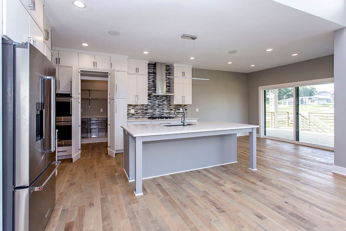 Kitchen interior with large island, white cabinets, pantry, and sliding glass door to deck.
