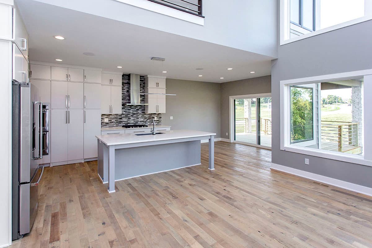 Open concept kitchen and living area with a large island, modern cabinetry, and expansive windows overlooking a deck.