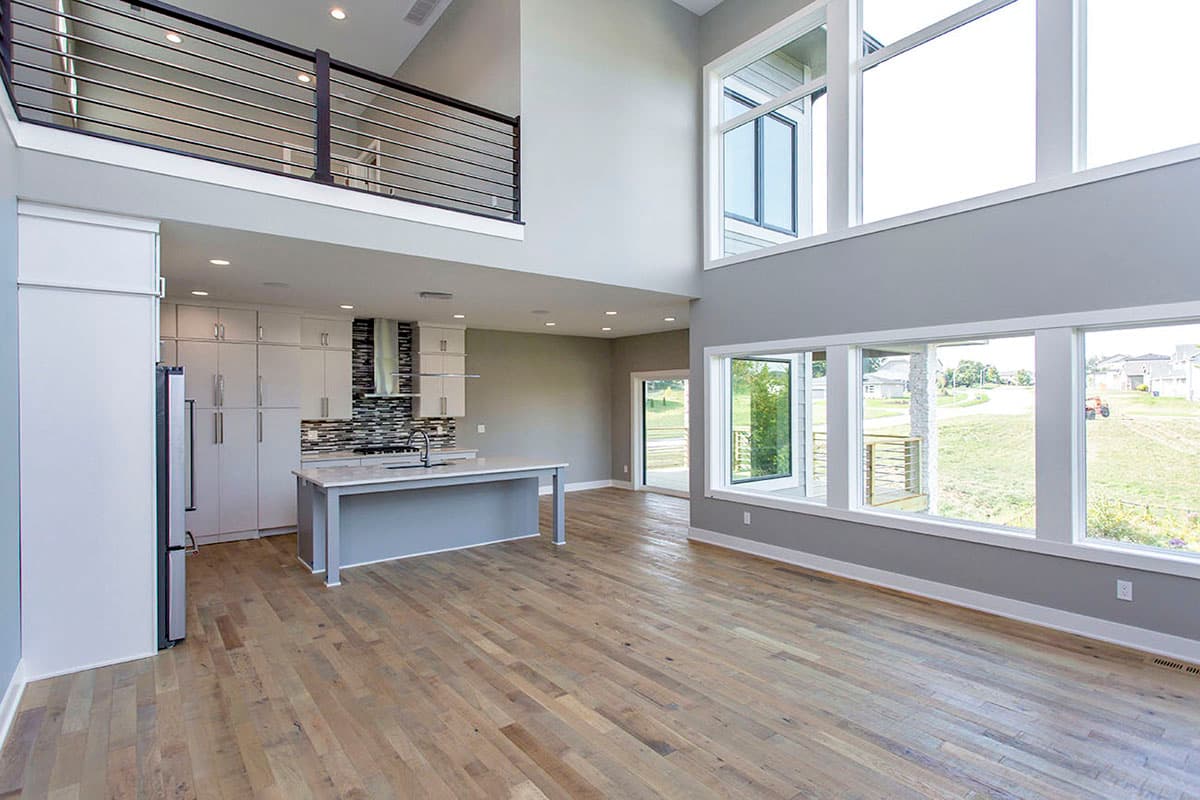 Open concept living area with kitchen, island, vaulted ceiling, loft railing, and large windows.