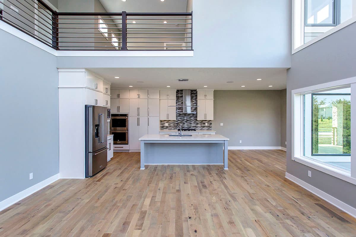 Modern open-plan interior with kitchen, island, and view of lofted hallway with metal railing.