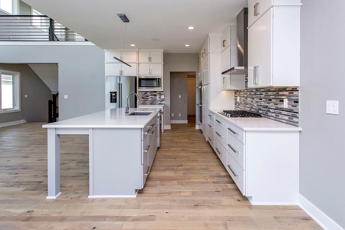 Modern kitchen interior with two islands, white cabinetry, stainless steel appliances, and a mosaic tile backsplash.