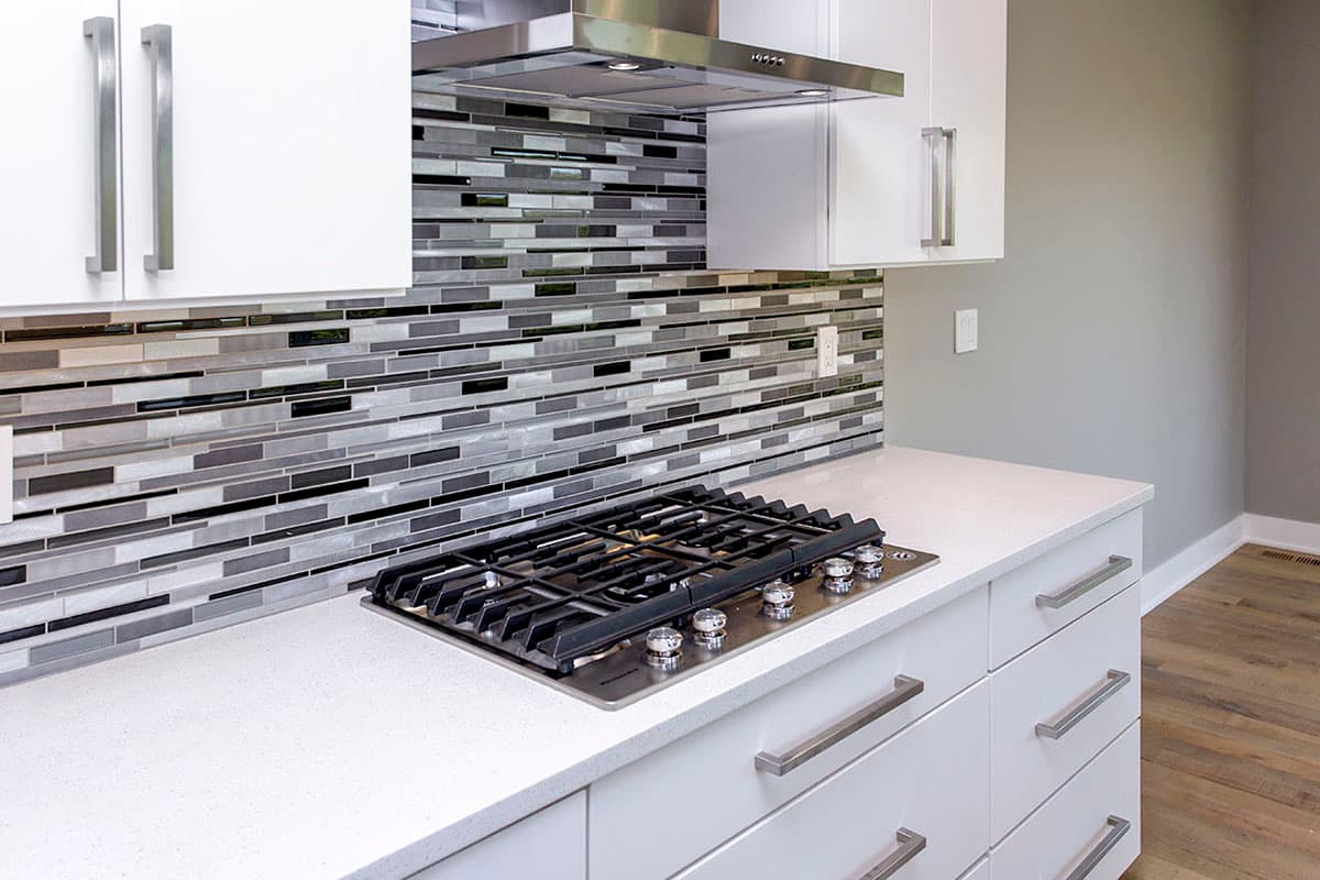 Kitchen with gas range, white quartz countertop, and linear glass mosaic tile backsplash.
