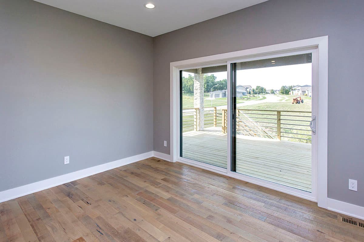 Interior view of room with hardwood floors and sliding glass doors opening to a wood deck with metal railings.