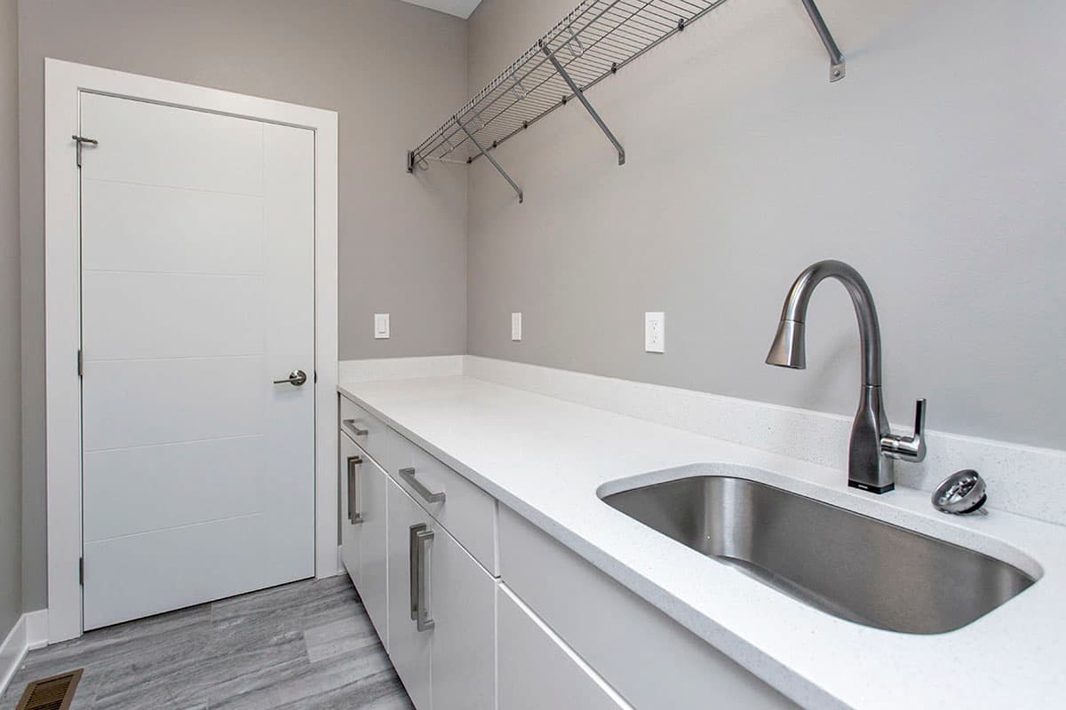 Laundry room with white cabinetry, countertop, sink, faucet, and a modern door.