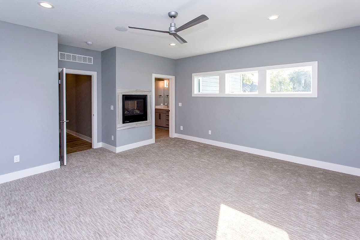 Spacious room with carpet, fireplace, ceiling fan, and a bank of three horizontal windows.