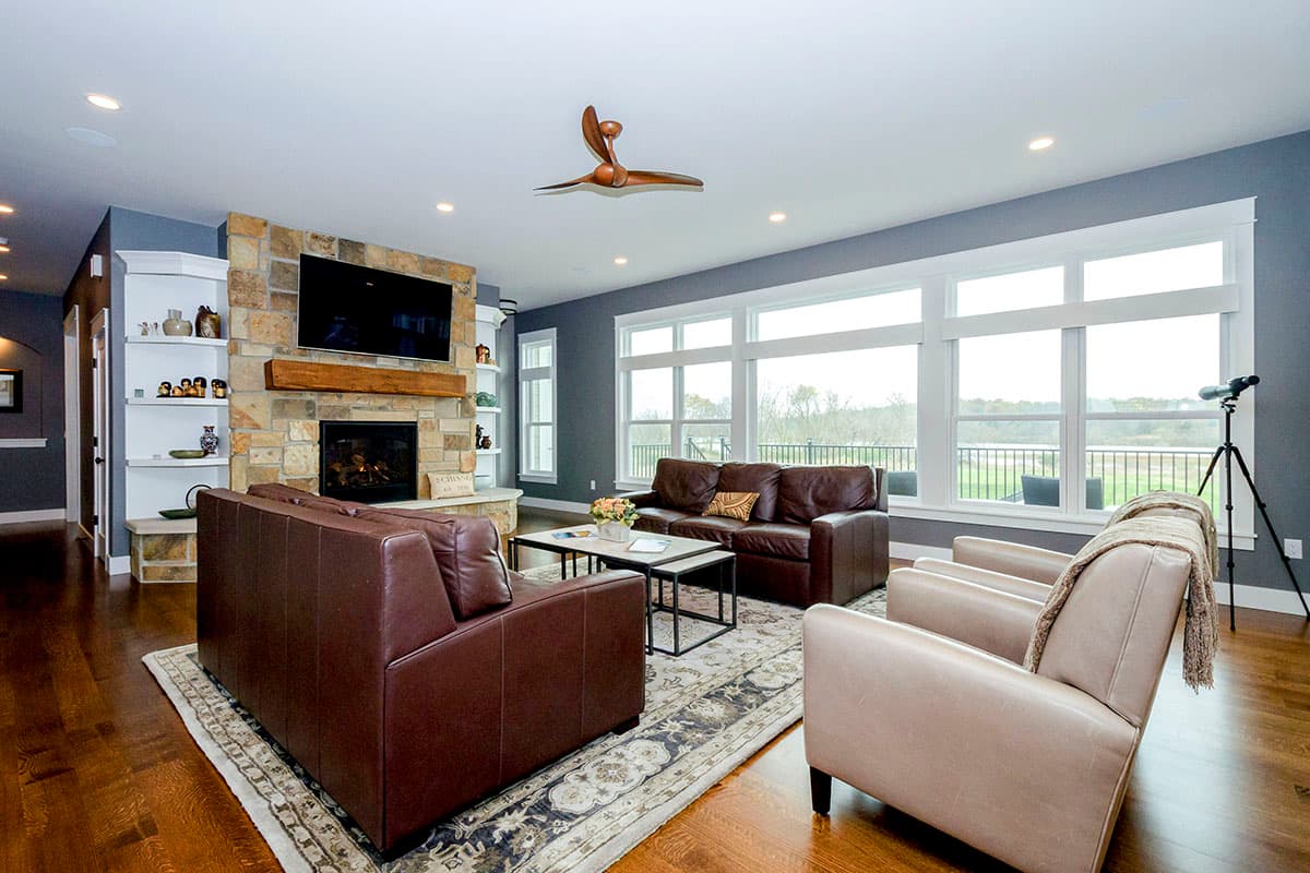 Living room with stone fireplace, built-in shelves, large windows, and leather seating.