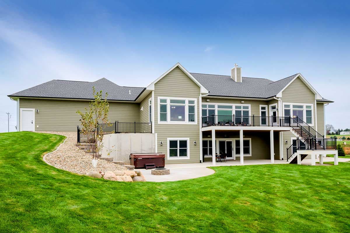 House plan exterior with prominent deck, large windows, gables, and attached garage on left.