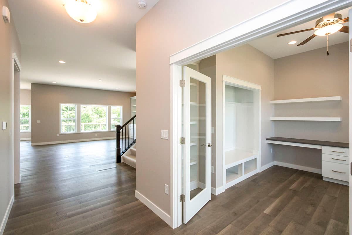 Interior view of a house plan showing an open living area with large windows, a staircase, and a built-in desk with shelving.