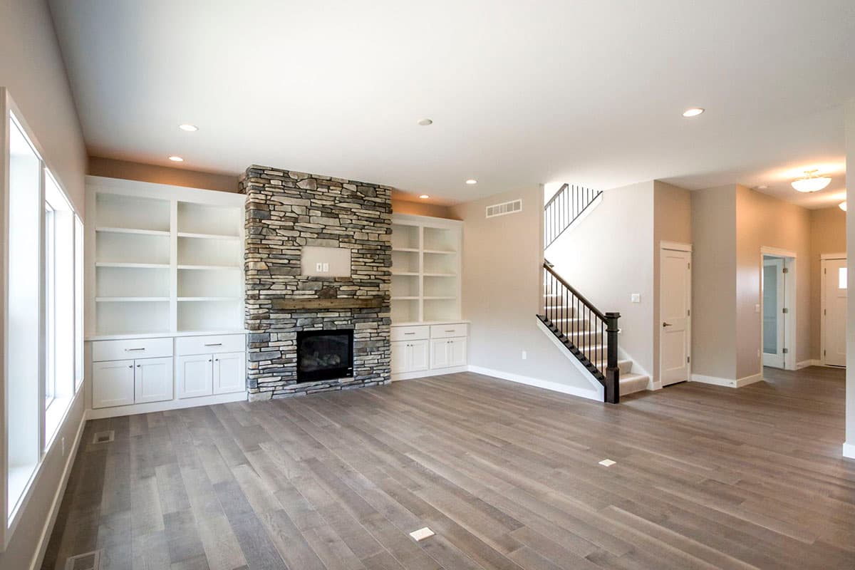 Great room with stone fireplace, built-in white shelving, wood flooring, and staircase.
