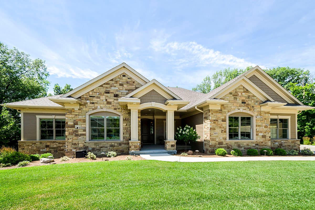 House plan exterior with stone veneer, gabled roof, and arched window. Features covered entry with columns and a well-manicured lawn.