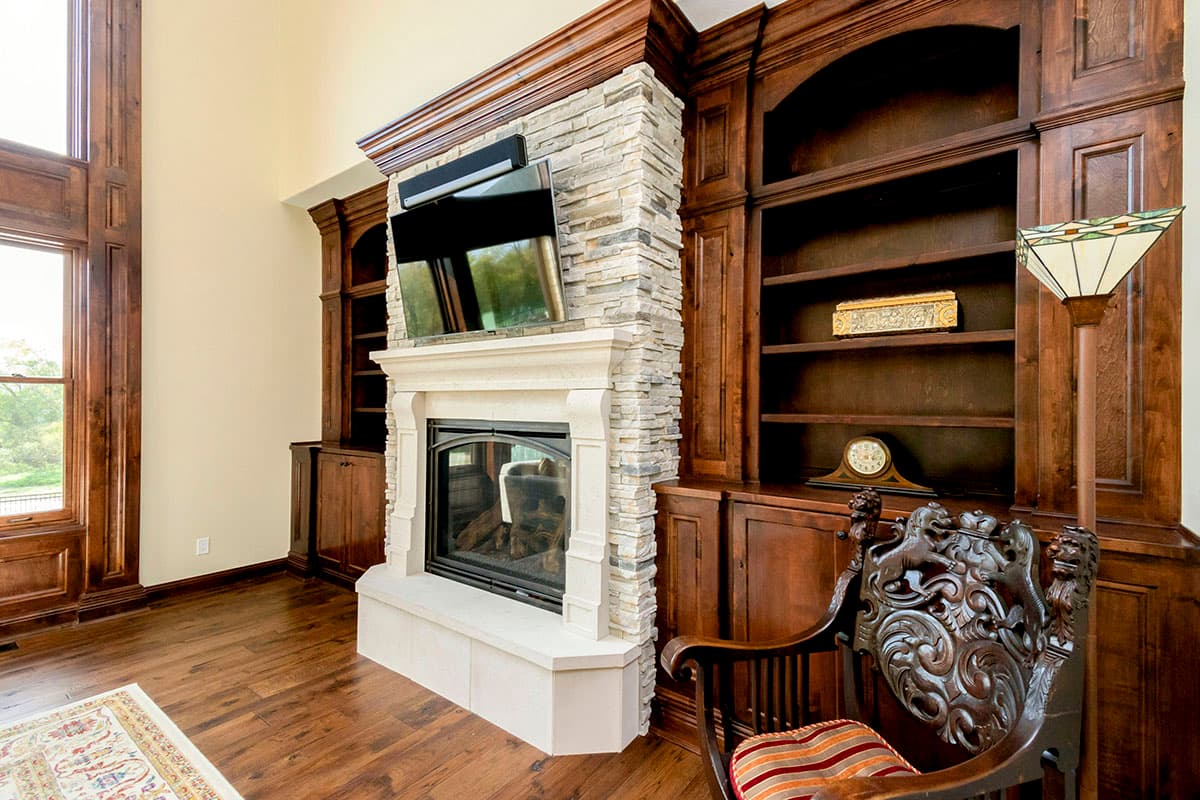 Living room with stone fireplace, built-in wood shelving, and large windows.