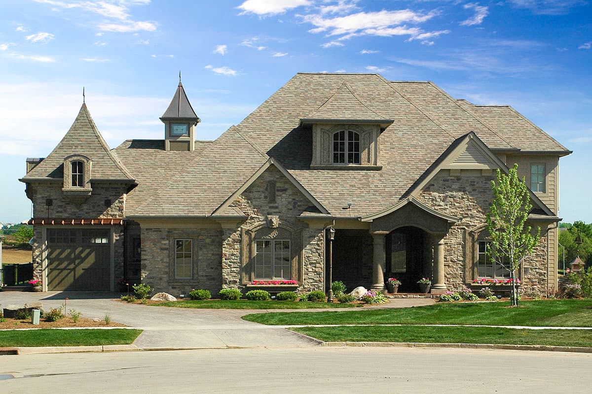 House plan exterior. Two-story, stone-clad French Eclectic style. Features include a hipped roof, dormers, a turret, and a covered front entry.
