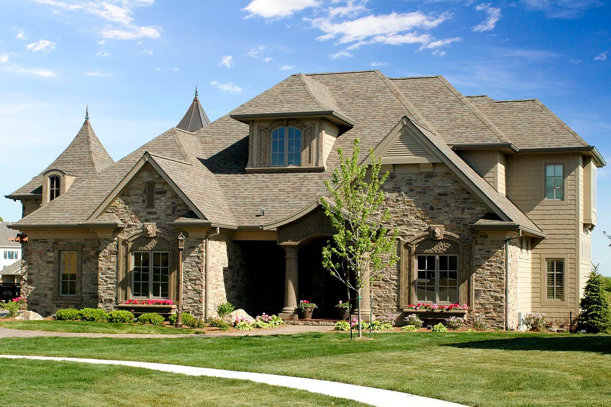 House plan exterior: Stone facade with multiple gables, dormers, and turrets. Covered entry with columns.