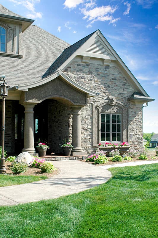 House plan exterior with stone facade, arched entry with columns, and decorative window surround.