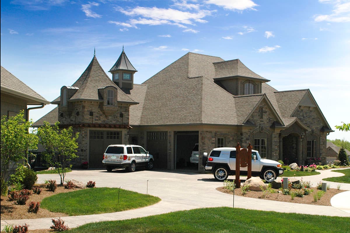 House plan exterior with stone facade, multiple gables, dormers, turrets, and a three-car garage.