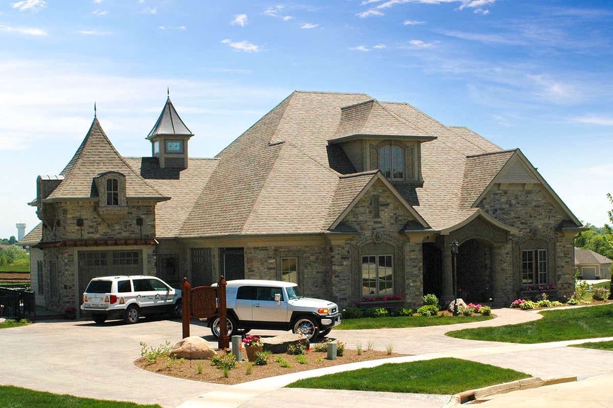 House plan exterior featuring stone facade, multiple gables, turret with spire, dormer windows, and attached garage.