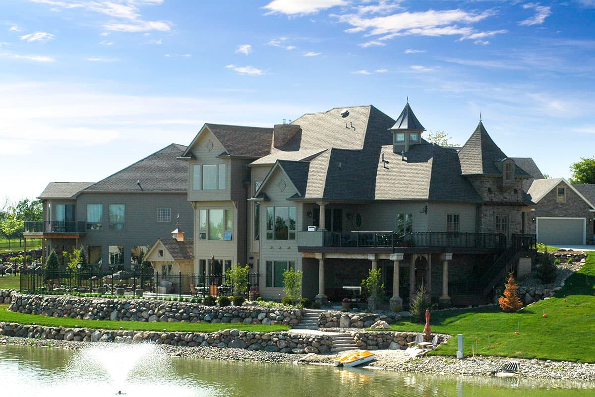 House plan exterior with multiple gables, turrets, covered balconies, and a lakeside setting.