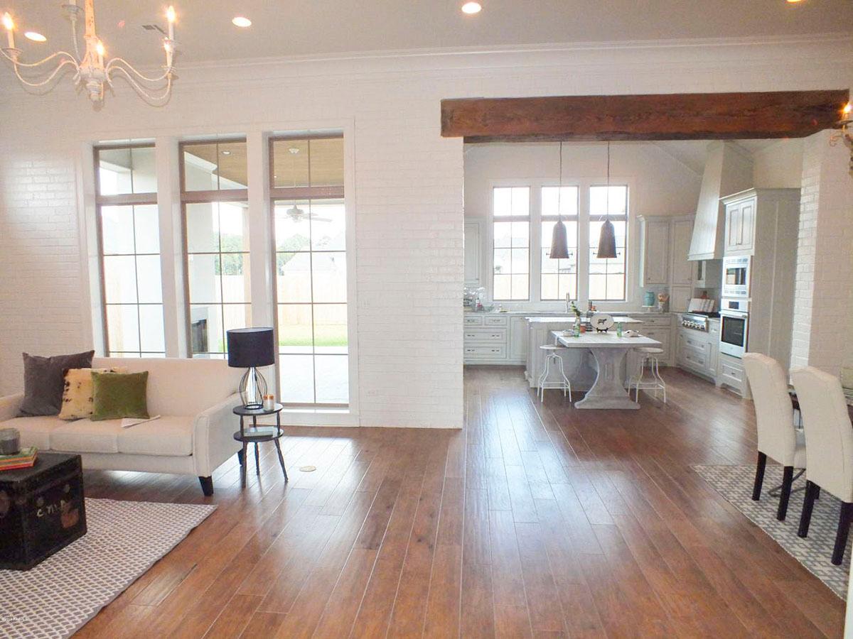 Open concept living space with a white sofa, large windows, and a kitchen with an island and white cabinetry.