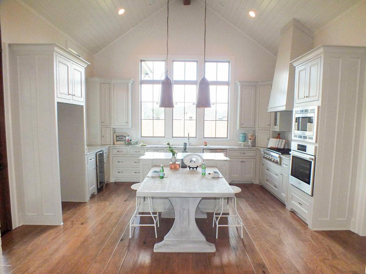 Kitchen with vaulted ceiling, central island, white cabinetry, and a large window bank.