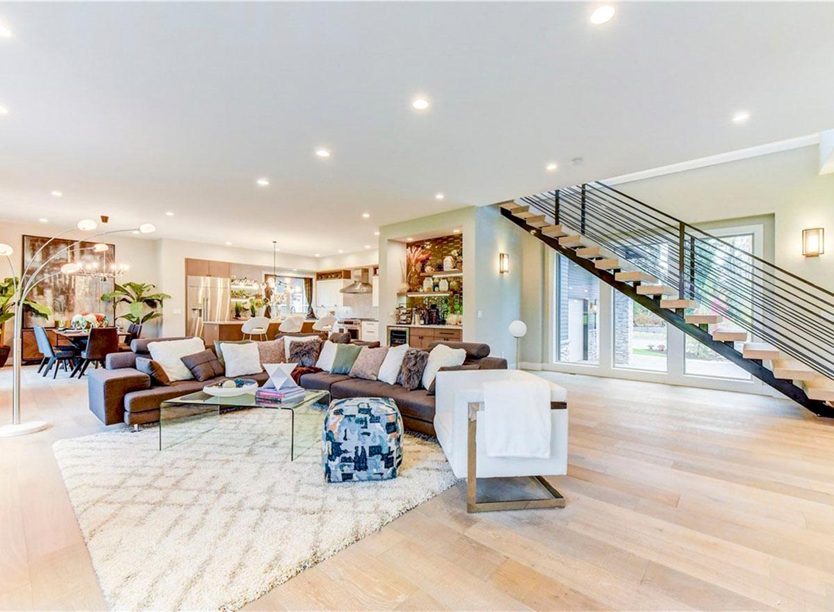 Modern open-concept living area with sectional sofa, floating staircase, and view of kitchen and dining areas.