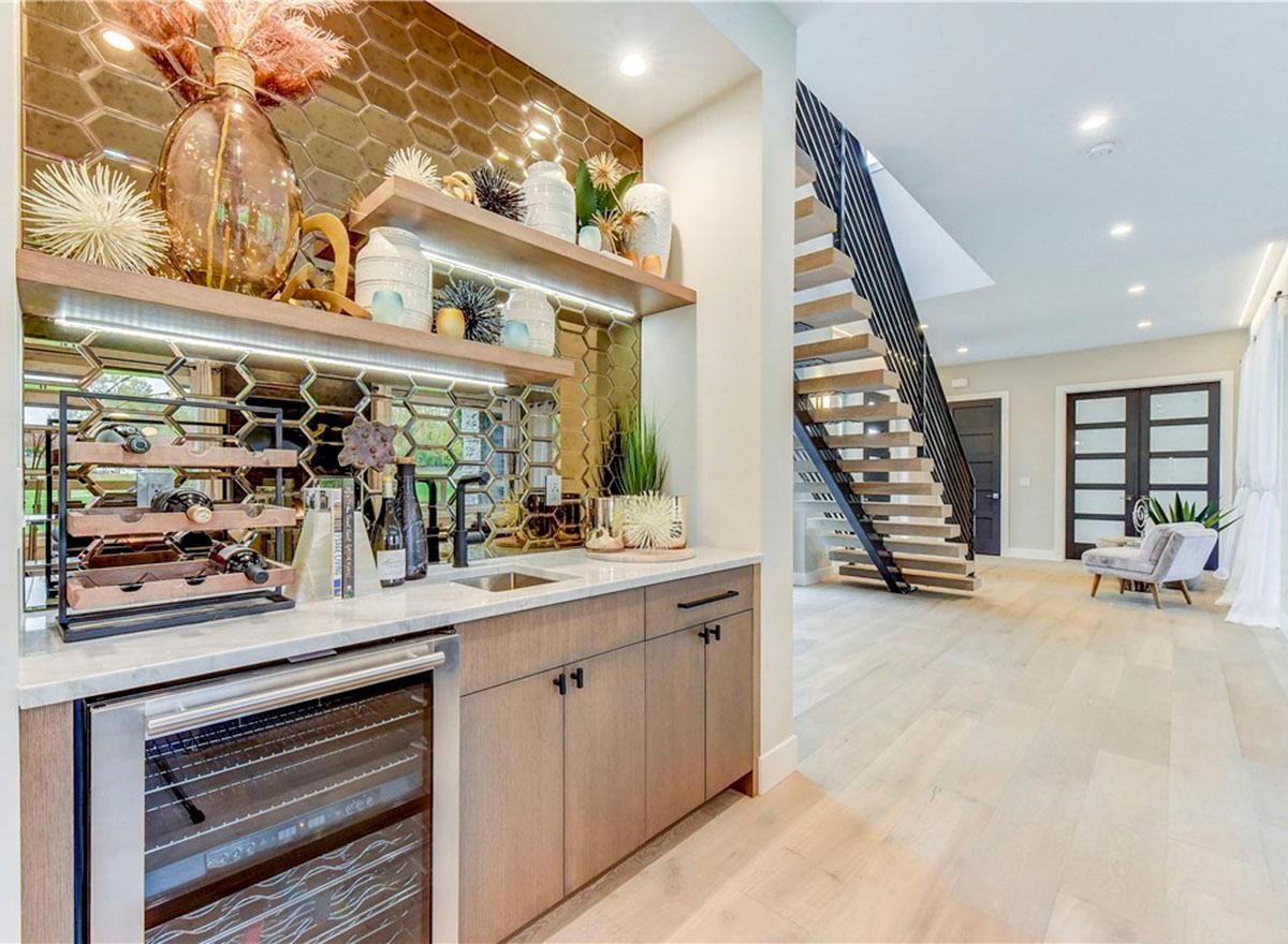 Interior view of a wet bar with wine fridge, sink, and honeycomb tile backsplash, adjacent to a modern floating staircase.