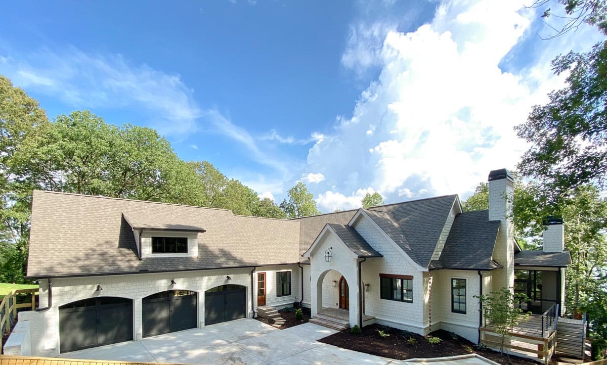 House plan exterior: Modern Farmhouse style, one-story with three-car garage, arched entry, and prominent chimneys.