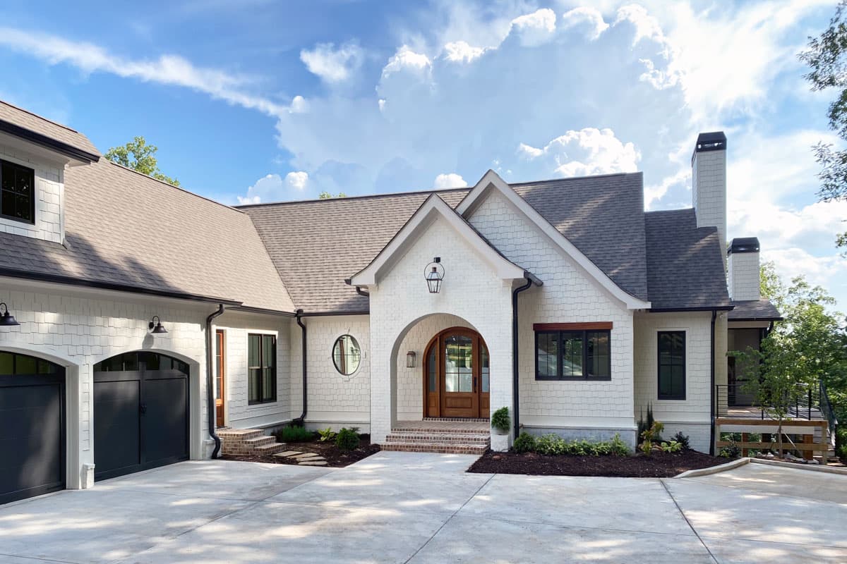 House plan exterior: Modern farmhouse style with gabled roof, arched entry, circular window, and double garage.
