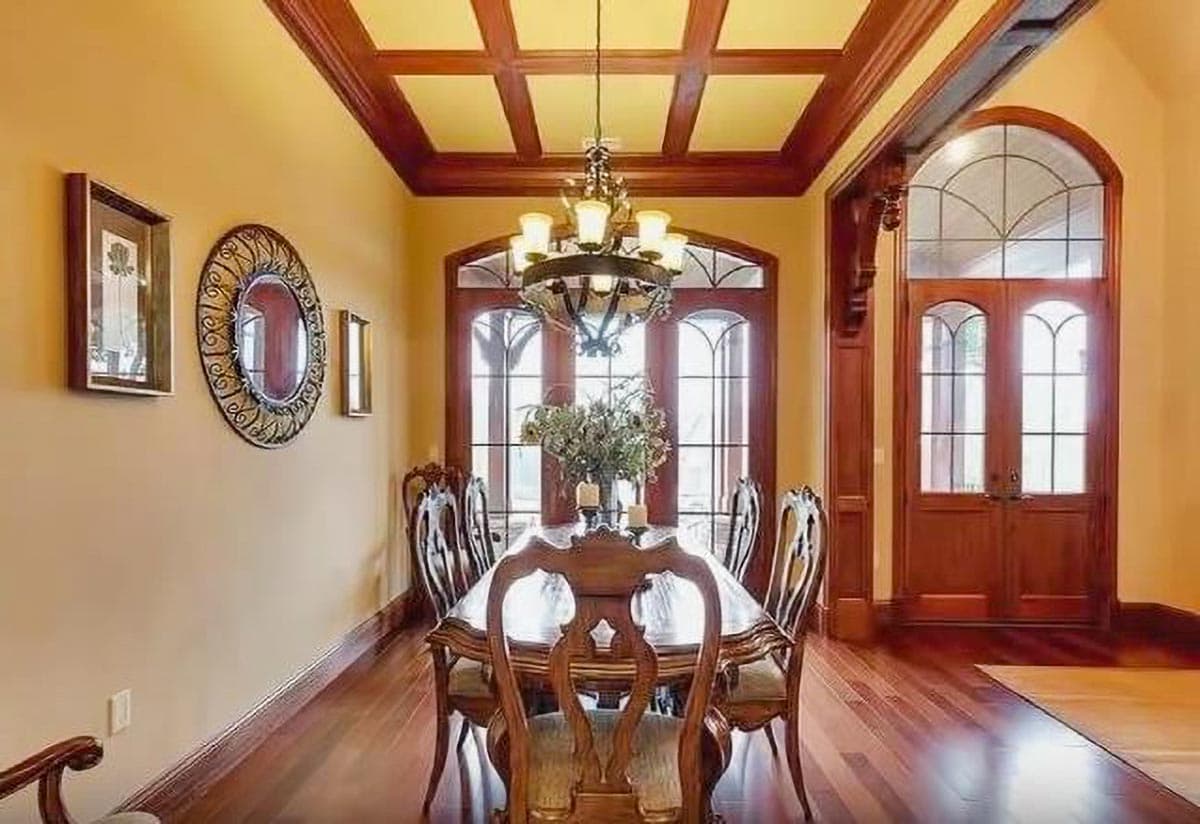 Formal dining room with coffered wood ceiling, arched windows, double doors with arched transoms, and ornate dining set.