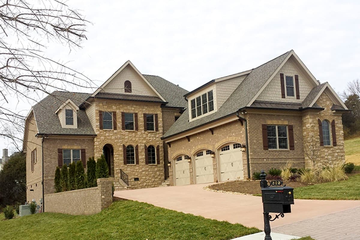 House plan exterior featuring a two-story design with stone and brick facade, multiple gables, dormers, and a three-car garage.