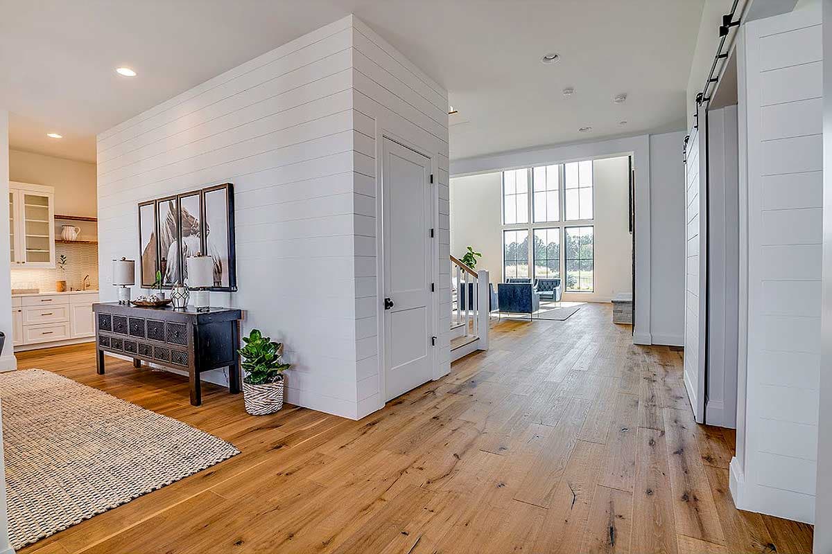 Interior view of modern house featuring shiplap walls, a kitchen with island, and a great room with a wall of windows.