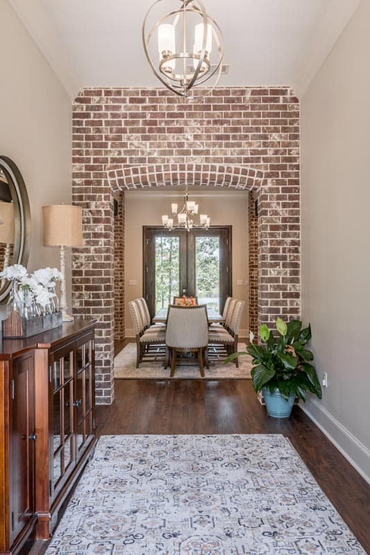 An arched brick doorway leads to a dining room with a table set for six. A buffet with decor and a potted plant flank the hallway.