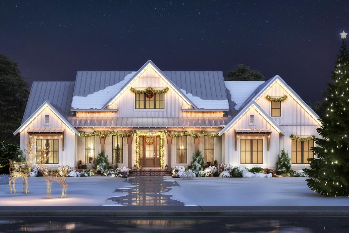 A white house at night, decorated for Christmas with lights, wreaths, and a Christmas tree. Snow covers the roof and ground, with illuminated reindeer.