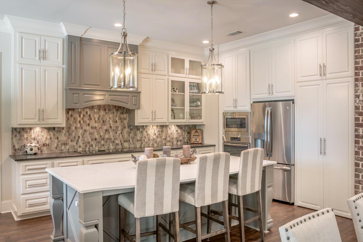 A modern kitchen features white cabinetry, a large island with striped bar stools, stainless steel appliances, and decorative pendant lights.