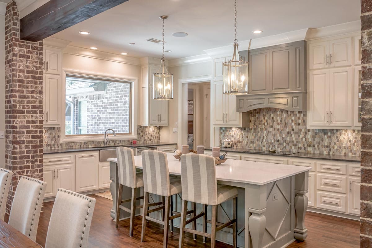 Spacious, bright kitchen with a large island, pendant lights, and bar stools. Features white cabinets, a brick accent wall, and wood flooring.