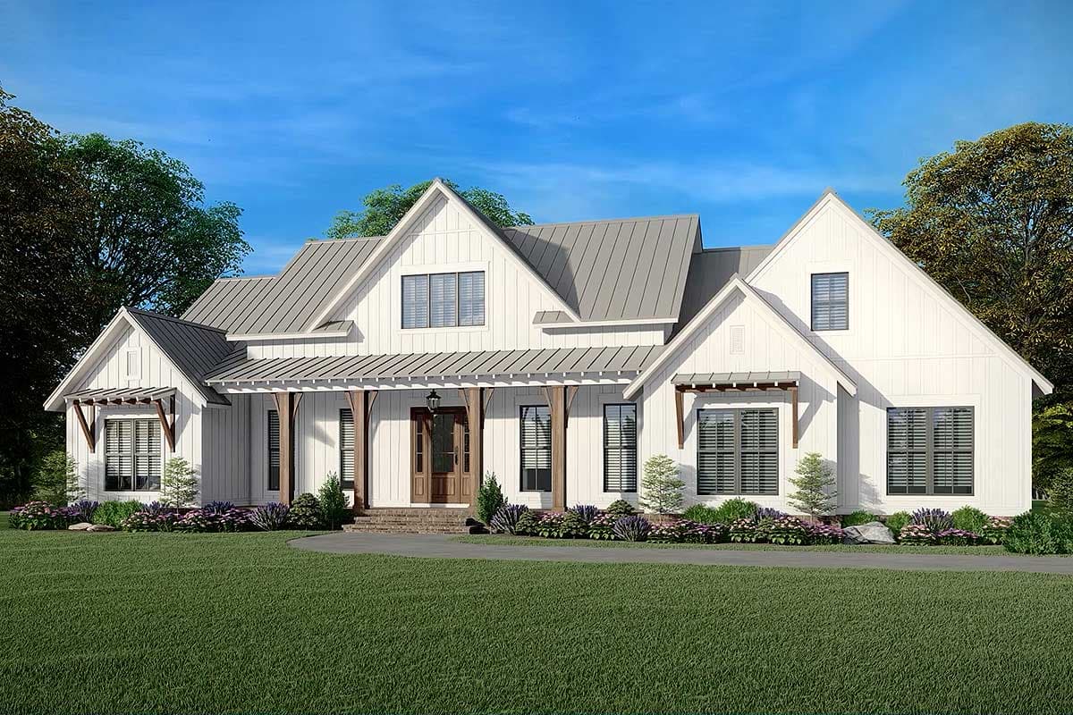A white, modern farmhouse with a grey metal roof and a large porch, set against a blue sky with green grass and landscaping.