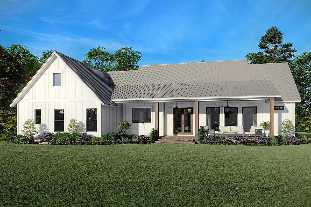 A modern white farmhouse with a metal roof, front porch, and large windows. Lush green grass and blue sky complete the serene setting.