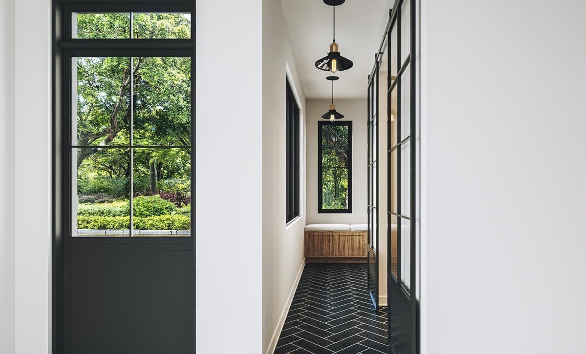 Hallway with large windows, herringbone tile floor, built-in bench, and black-framed sliding doors.