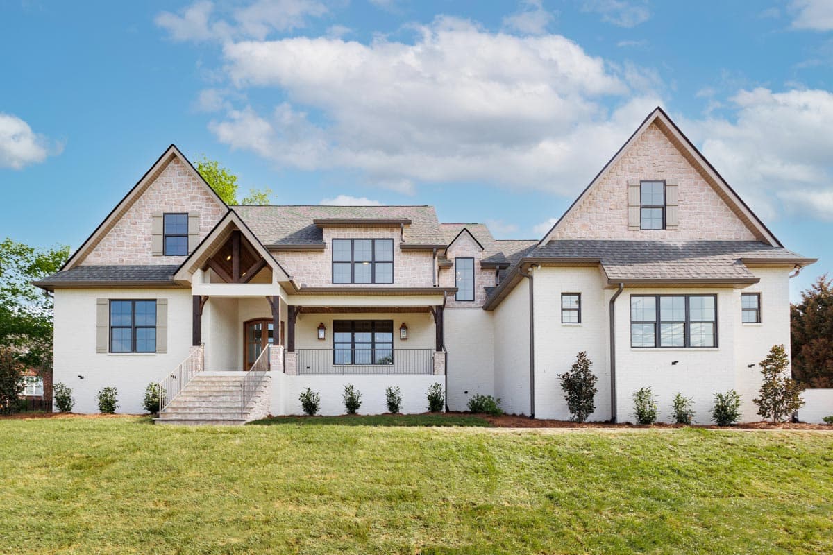 House plan exterior. Two-story, Modern Farmhouse style with a gabled roof, stone accents, and a covered porch. Brick exterior.