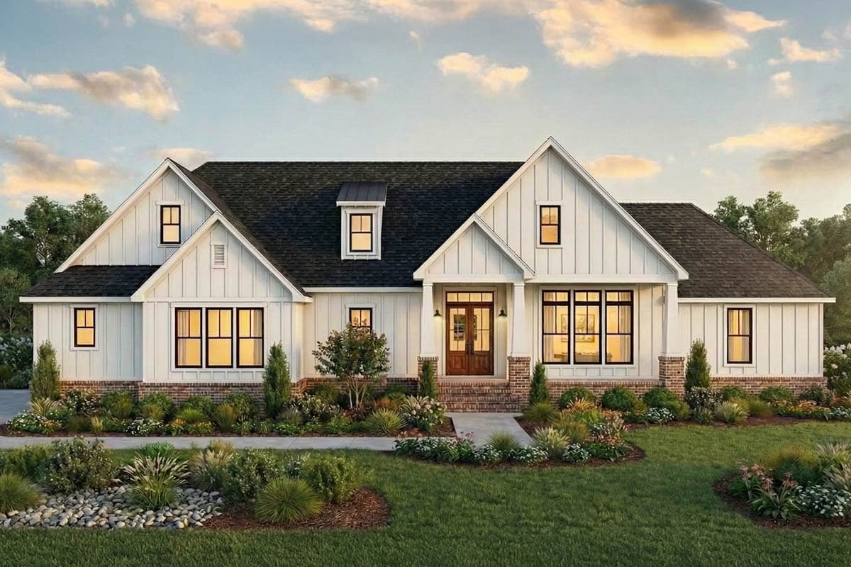 A white farmhouse with a dark roof and black window frames is set against a blue sky with fluffy clouds and well-manicured landscaping.